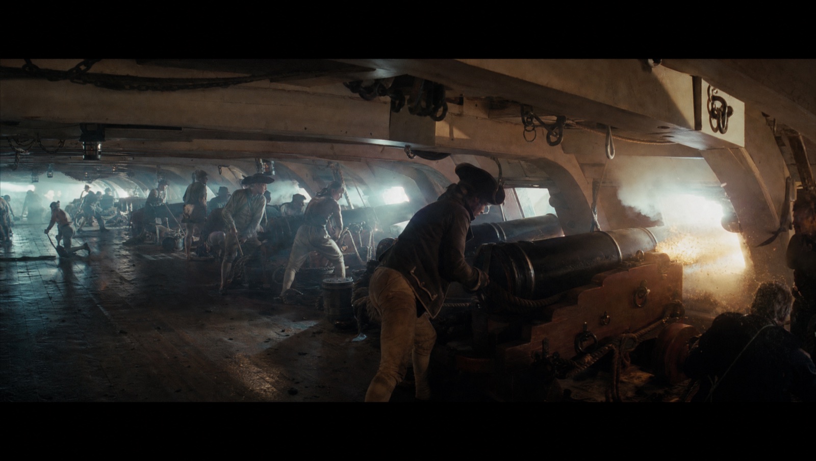 A gun crew works around a 32-pounder in the smoky half-light of a wooden lower deck.